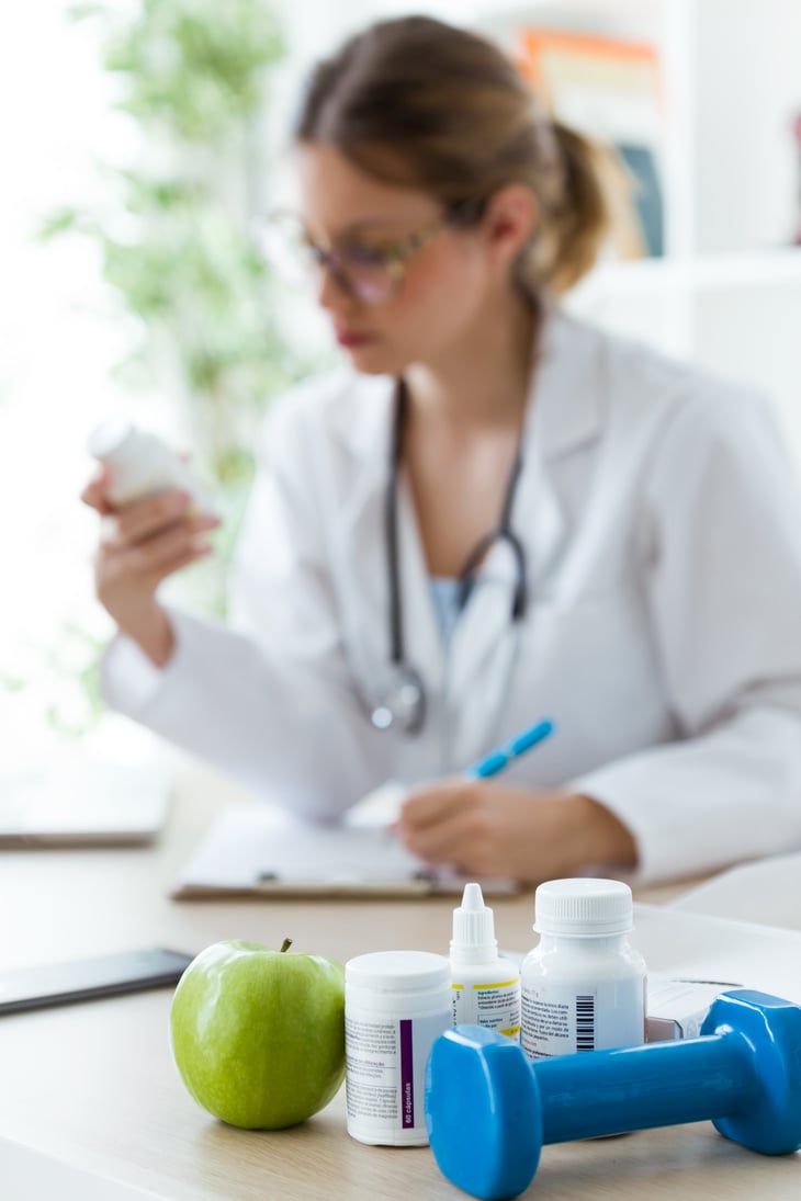 Female Dietician Holding a Nutritional Supplement While Writing